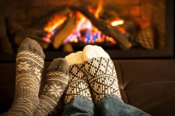 Image of two people’s feet warming next to a fireplace