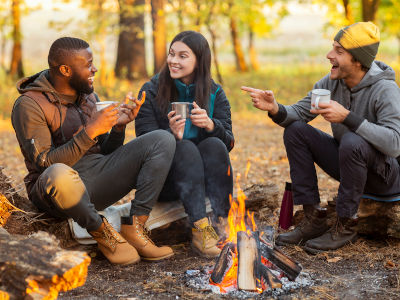 Friends sitting beside fireplace in autumn forest, enjoying time together