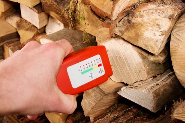 A person uses a moisture meter to test the moisture content of firewood