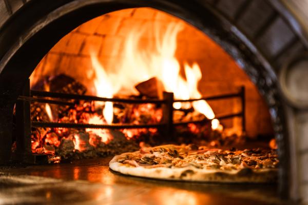 A fresh pizza sits beside the fire that baked it