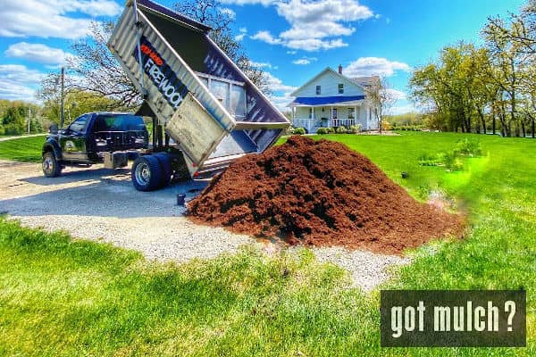 A truck dumps a pile of mulch on the ground