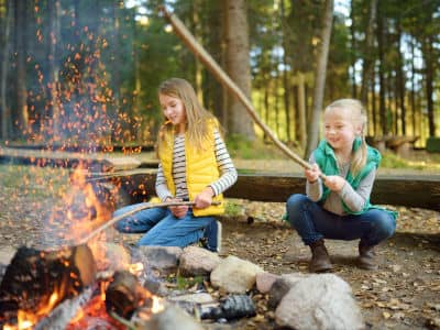 A picture of two girls roasting marshmallows over burning firewood.