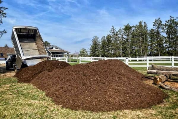 Photo of brown bulk mulch being delivered to a fenced in field.